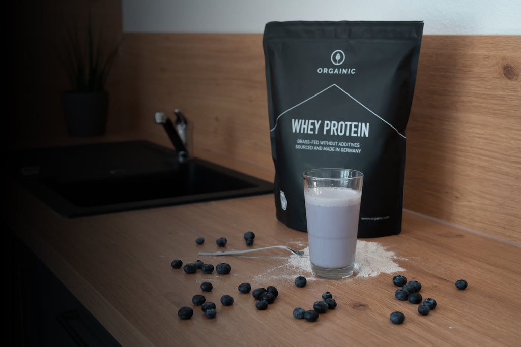 ORGAINIC Whey Proteinpulver am Tisch mit Glas